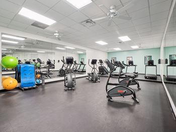 A gym with a variety of exercise equipment including treadmills, stationary bikes, and weights.
